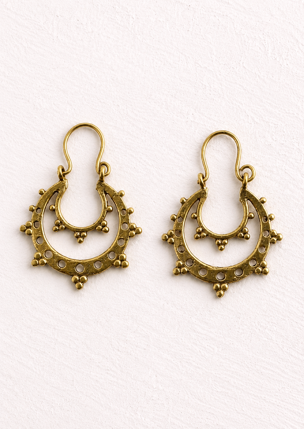 Delicate gold-coloured crescent hoop earrings with open cut-out detailing and mini bead accents. Placed on a white Background. 
