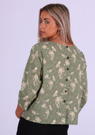 Woman stands showing the back of the cotton top she is wearing with decorative buttons down the centre of the back