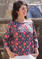 Model in a cotton relaxed fit 3/4 sleeve top in a red and green floral print on a blue base 
