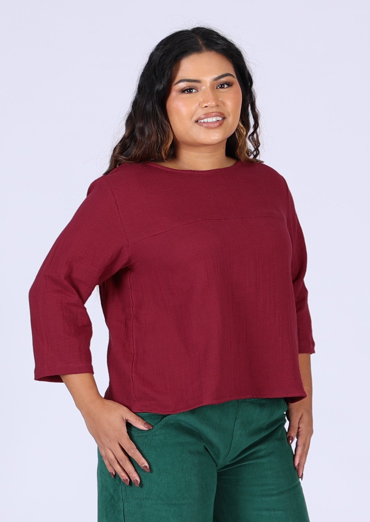 Model wears deep warm red double cotton top with 3/4 sleeves and high round neckline
