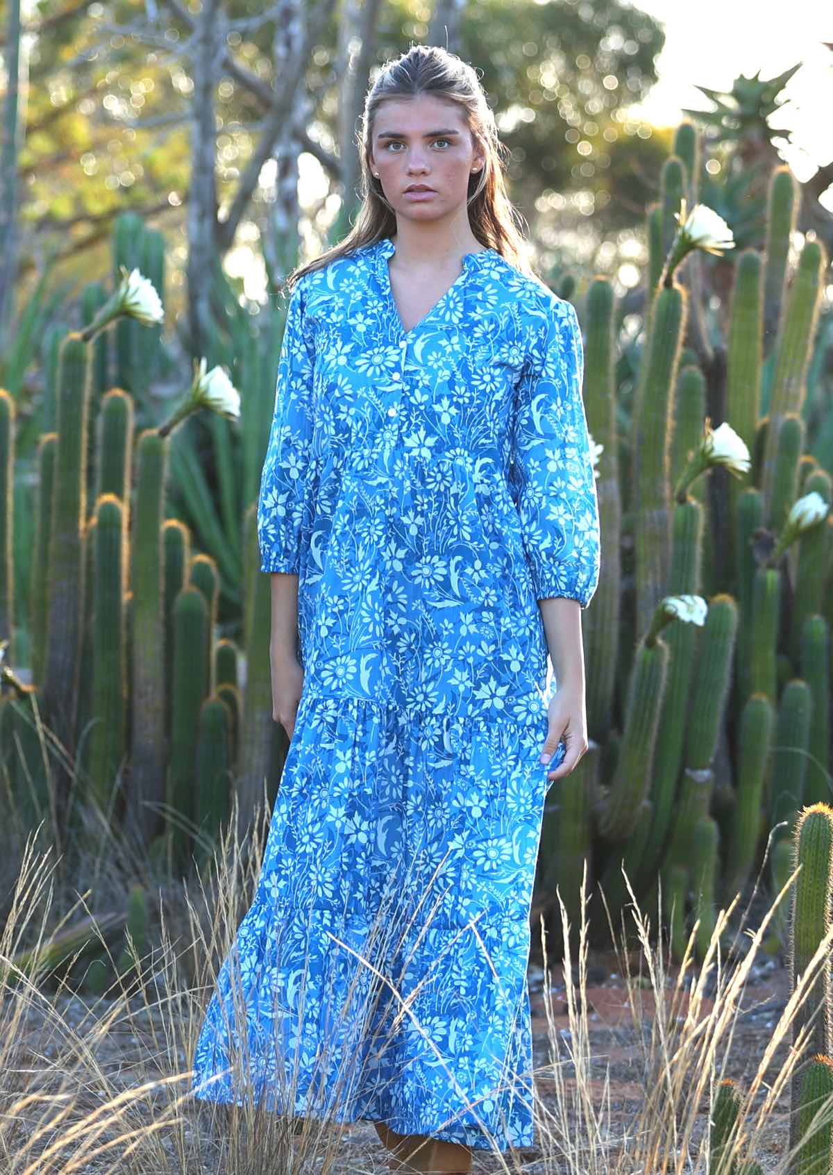 woman in blue cotton maxi dress with light blue and white floral print in front of cactus 