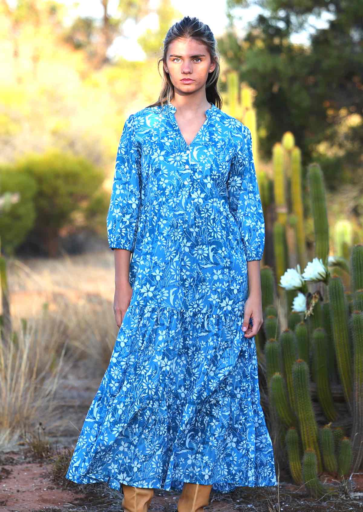 woman in blue cotton maxi dress with light blue and white floral print in front of flowering cactus 