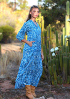 woman in blue cotton maxi dress with light blue and white floral print with hand in pockets
