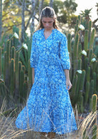 woman in blue cotton maxi dress with light blue and white floral print holding full skirt out