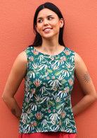 Model leans on wall in sleeveless cotton top with earthy coloured floral on a dark green base