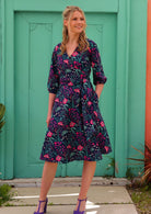 Blonde woman in long sleeve navy and purple floral cotton wrap dress in front of aqua door