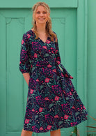 Blonde woman in long sleeve navy floral cotton wrap dress in front of aqua door