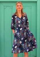 woman with blonde hair in 100% cotton wrap dress in blue with white flowers and long sleeves in front of aqua door