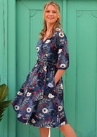 woman in 100% cotton wrap dress in blue with white flowers and long sleeves in front of aqua door