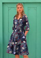 woman in 100% cotton wrap dress in blue with white flowers and long sleeves in front of aqua door