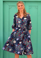 woman in 100% cotton wrap dress in blue with white flowers and long sleeves  with pockets in front of aqua door