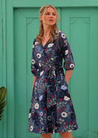 woman in cotton wrap dress in blue with white flowers and long sleeves in front of aqua door