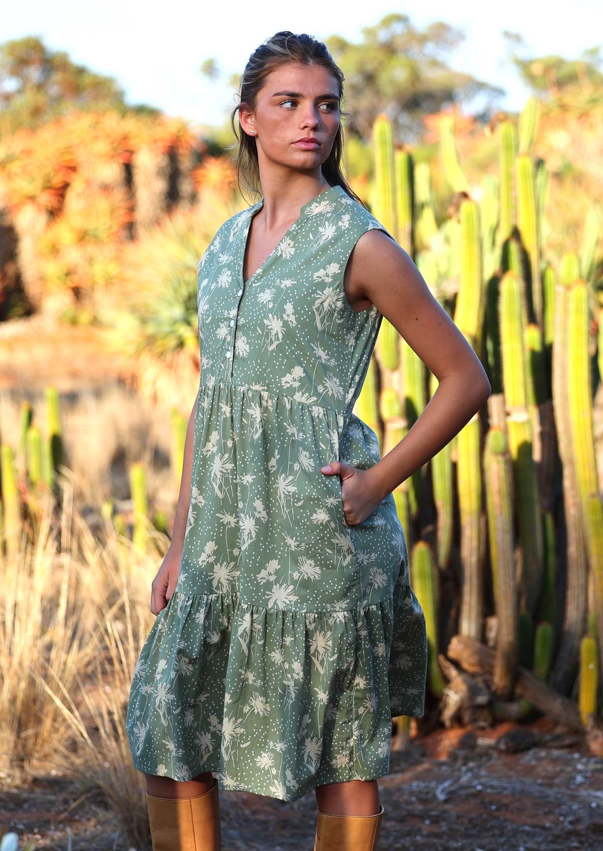 Woman wears cotton sleeveless dress with cream floral silhouettes on a pale green base