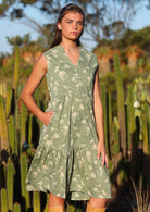 Model wears cotton sleeveless sun dress with buttoned bodice and V-neckline in pale green with cream floral print