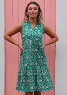 Woman stands in jade green base floral print cotton sleeveless dress with buttoned bodice and V-neckline