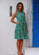 Woman stands in cotton jade green based floral print sleeveless dress with hand in hidden side pocket