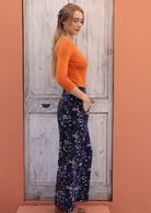 Model posing sideways wearing a beautiful printed wide leg corduroy pants with wide waistband and pockets.