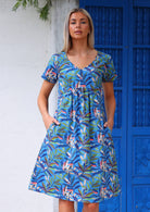 Woman stands with hands in pockets of cotton over the knee length dress with V-neckline ad short sleeves