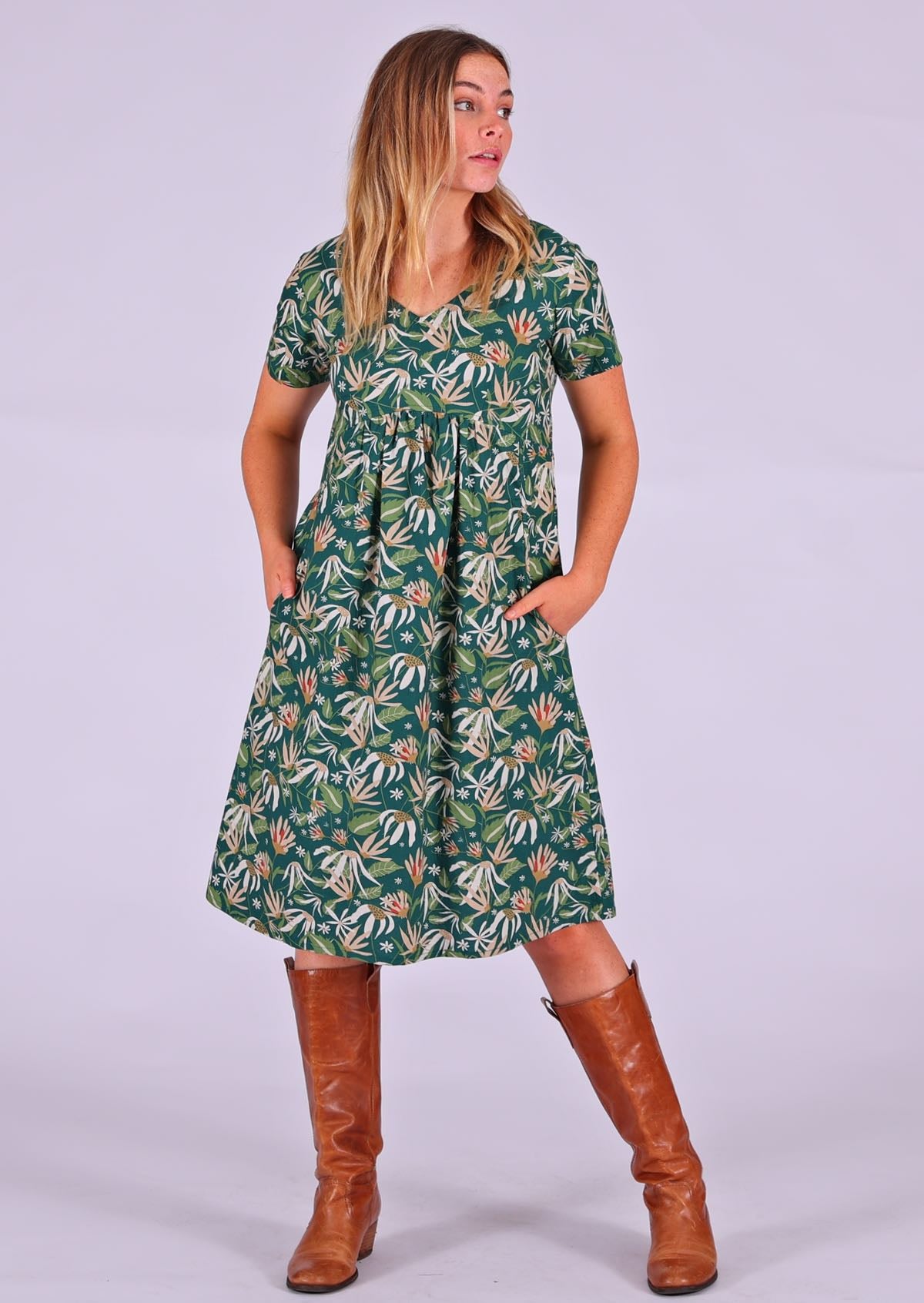 Model standing with hands in pockets modelling the Etta v-neck Dress Flannel Flower cotton green sundress with short sleeves paired with tan leather boots