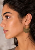 Close up of a woman wearing a beautifully detailed gold coloured earring. Featuring a curved crescent shape with ornate floral detailing. The embossed flower and leaf design gives them a lovely handcrafted feel and an earthy, antique-style finish.