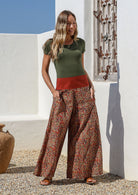 Woman wearing a green top and wide legged patterned cotton pants standing with her hands in her pockets 