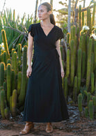 Woman wears black long wrap dress which forms a V-neckline, secured with a long waist-tie