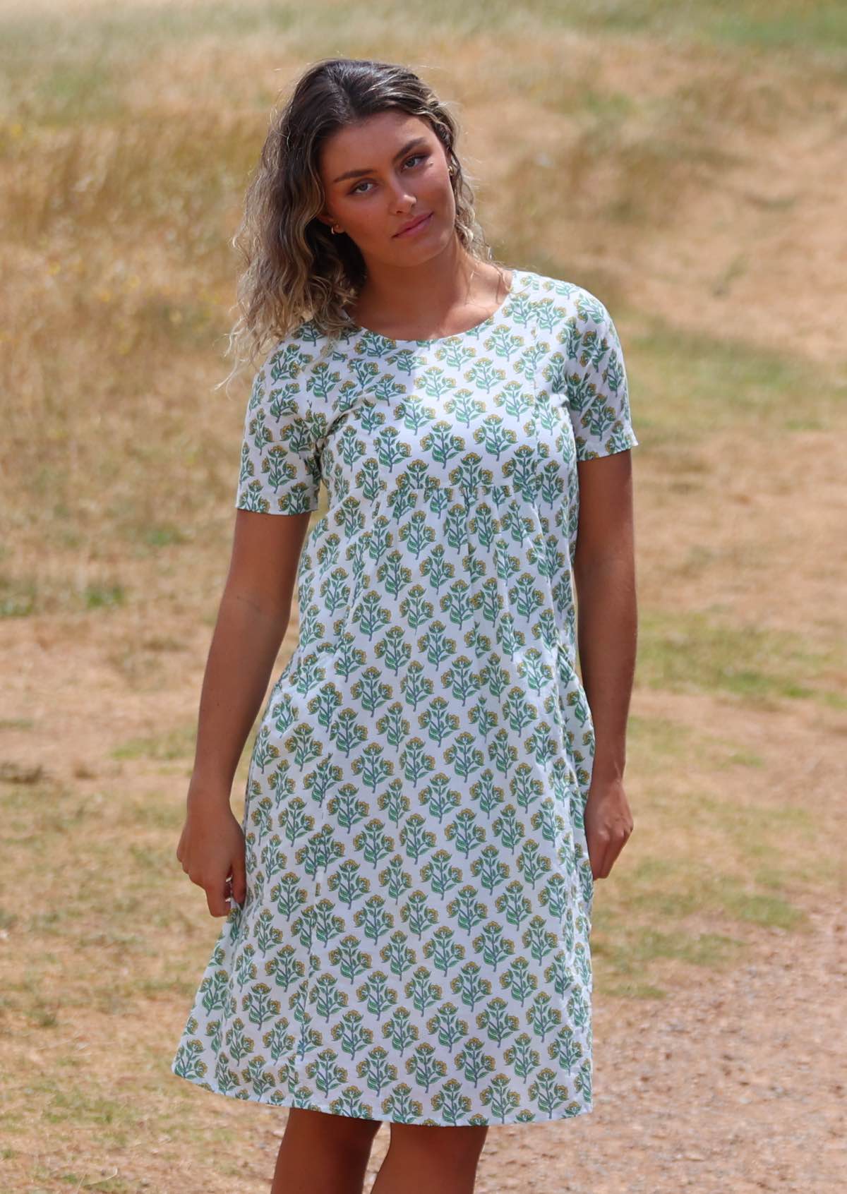 Woman wearing white cotton dress with floral pattern on top of hill 
