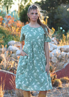 Woman stands with hand in pocket of cotton relaxed fit short sleeve dress in pale green