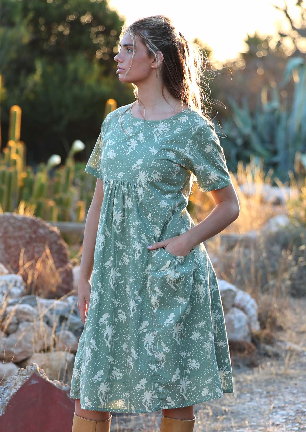 Woman stands sideways in cotton dress with gathers under the bust and front pockets