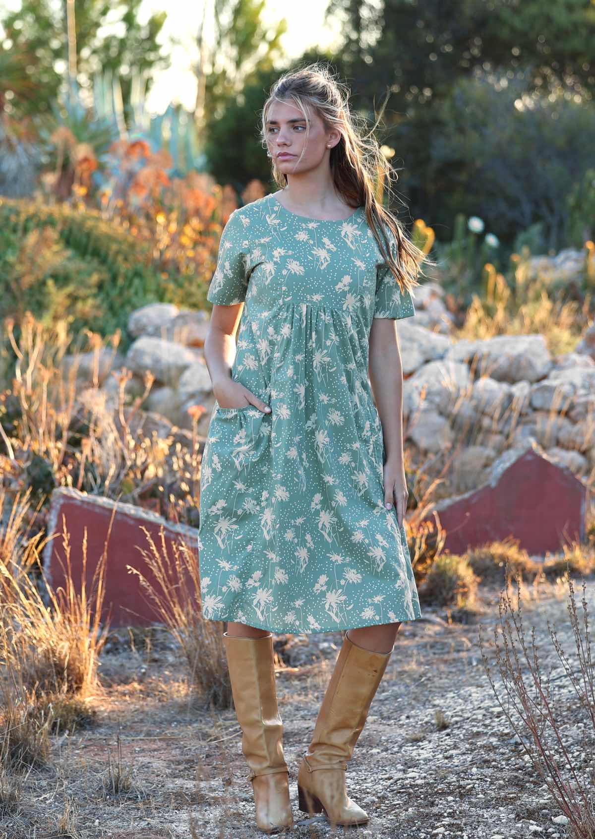 Woman wears cotton over the knee relaxed fit dress with empire waistline, with her hand in pocket