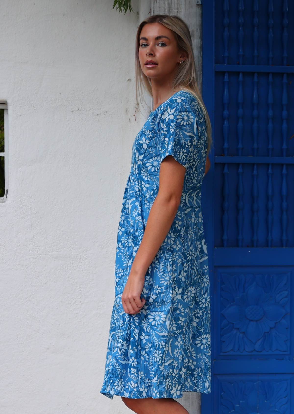 Woman stands sideways in cotton over the knee dress in blue floral print