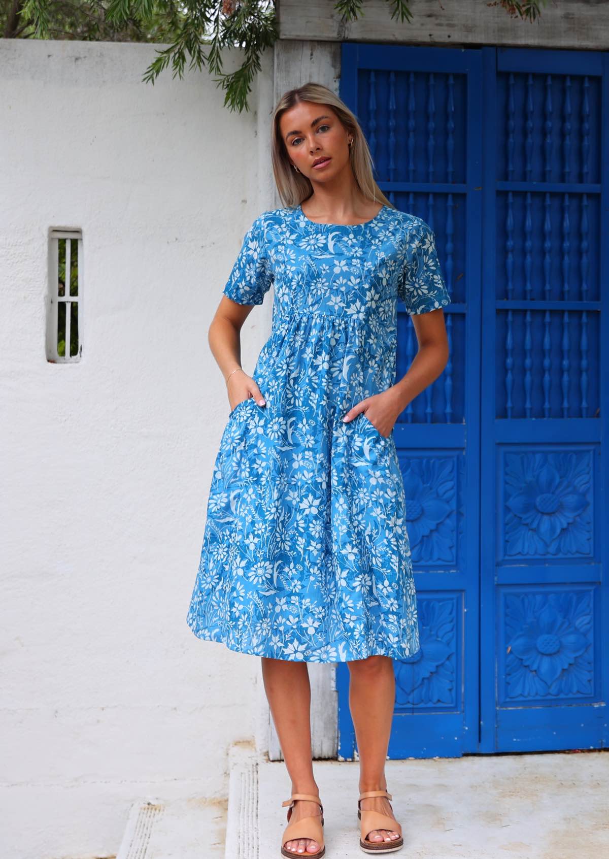 Woman stands in cotton relaxed fit dress that sits over the knee with hands in pockets