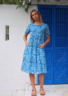 Woman stands in cotton relaxed fit dress that sits over the knee with hands in pockets