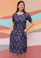 Woman in Indian print cotton dress with hands pockets in front of sun mural