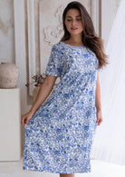 Woman wearing a blue floral cotton dress, 100% cotton, knee length in a neutral setting.