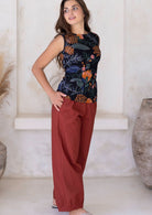 Woman stands sideways with hands in pockets, wearing relaxed-fit cotton pants in rust paired with a floral print cotton top