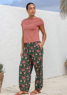 Model stands with a hand in pocket wearing 100% cotton floral print pants in deep green.