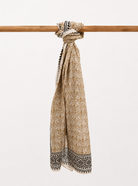 Beige patterned cotton scarf tied around a wooden stick on a white background