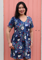 Model wear bold blue floral print cotton dress with short sleeves and V-neckline with hands in pockets