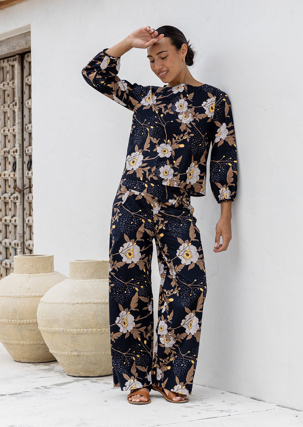 Model wears matching cotton top and pants featuring high waist, side zipper and pockets in black based floral print