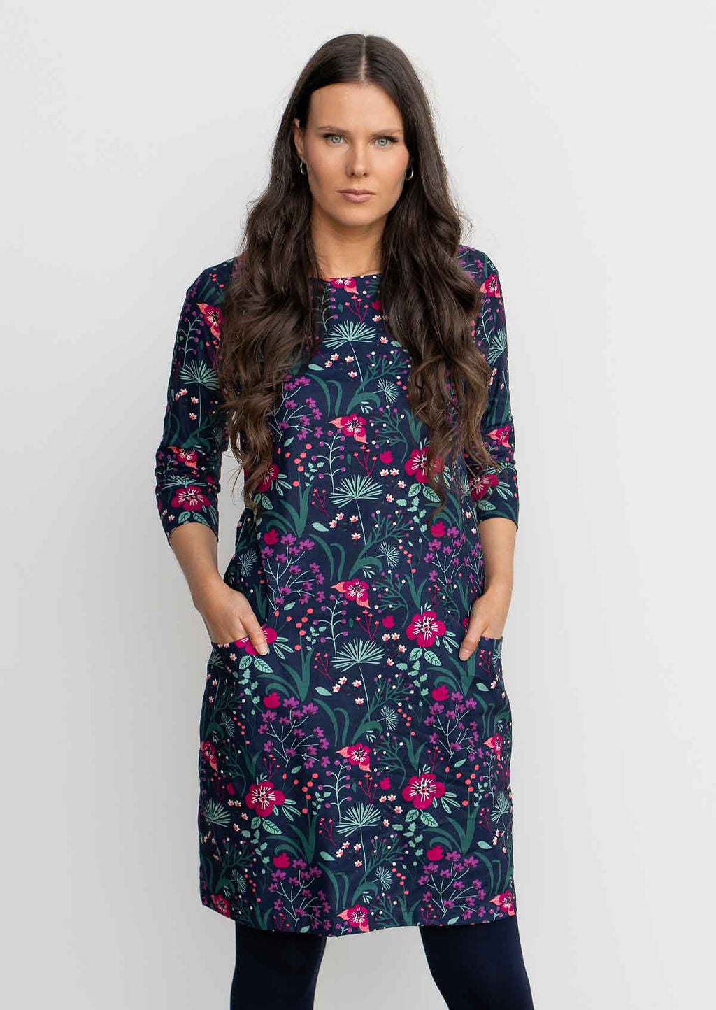 Woman leaning against wall wearing Cotton 3/4 sleeve shift dress with detailed cuff, in gorgeous floral print on dark blue base over navy blue leggings 