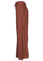 Side view of lightweight wide leg cotton pants in rust shade with drawstring waist tie and elastic back waist