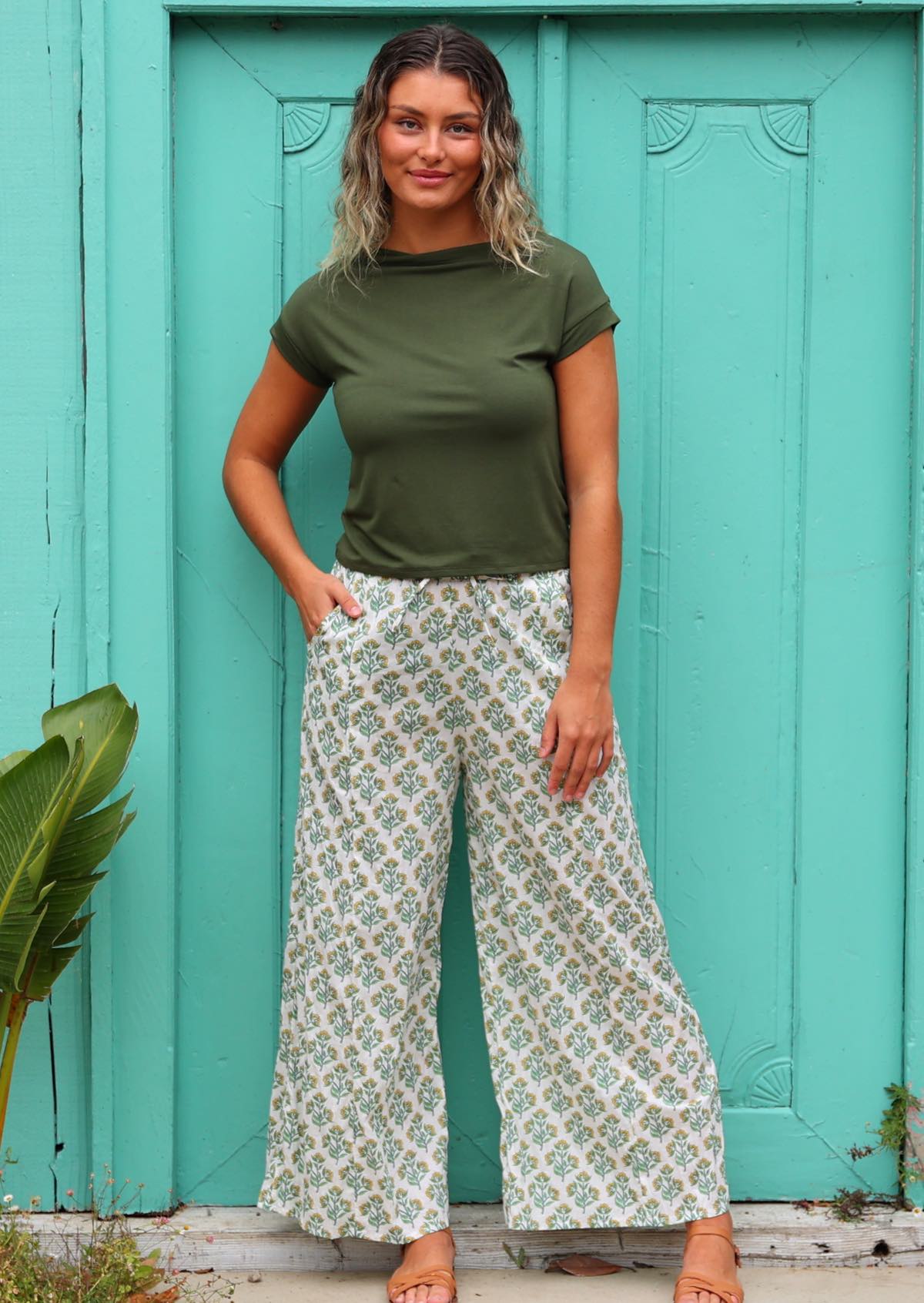 woman wearing white cotton palazzo pant with floral detail in front of aqua door with hand in pocket