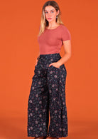 Model standing side on wearing Janis Pant Eventide 100 percent cotton wide legged women's palazzo with hands in pockets