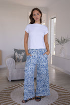 Woman wearing a white basic top and white based blue floral pants in a living room.
