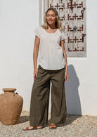 Woman wearing a lightweight olive green cotton pants with pockets, drawstring tie and elastic back waist.