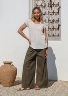 Woman poses in 100% cotton wide leg pants in olive green with drawstring waist tie and elastic back waist.