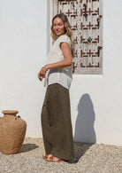 Woman standing sideways wears 100% cotton, relaxed wide leg cotton pants in olive green paired with short sleeved white cotton top 