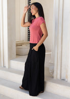 Woman in pink top paired with wide leg black rayon pants, with hand in pocket, standing on steps