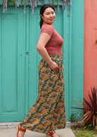 Model standing side on in front of aqua door with hands in pockets wearing rayon palazzo pant with pockets